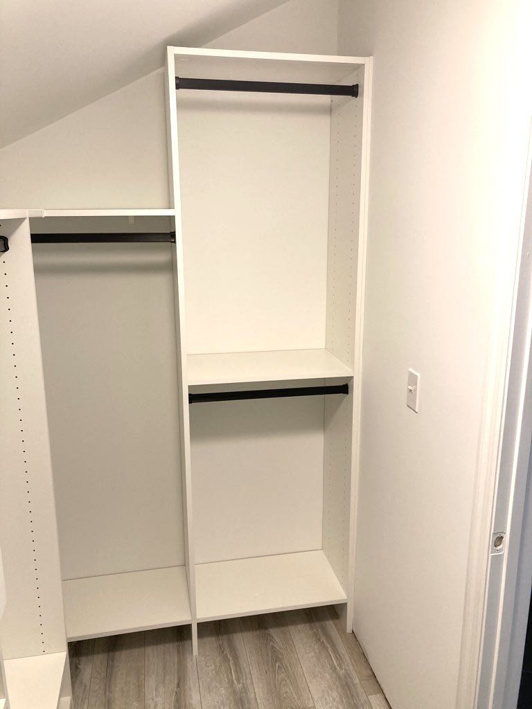 A walk in closet with a slanted ceiling and a white shelf.