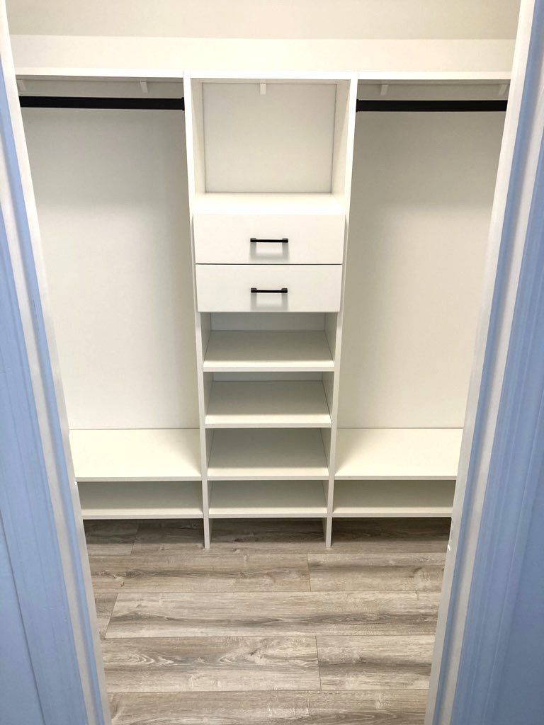 A walk in closet with a wooden floor and white shelves and drawers.