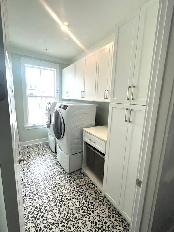 A laundry room with white cabinets , a washer and dryer , and a window.