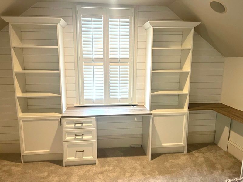 A room with a desk , shelves and a window.