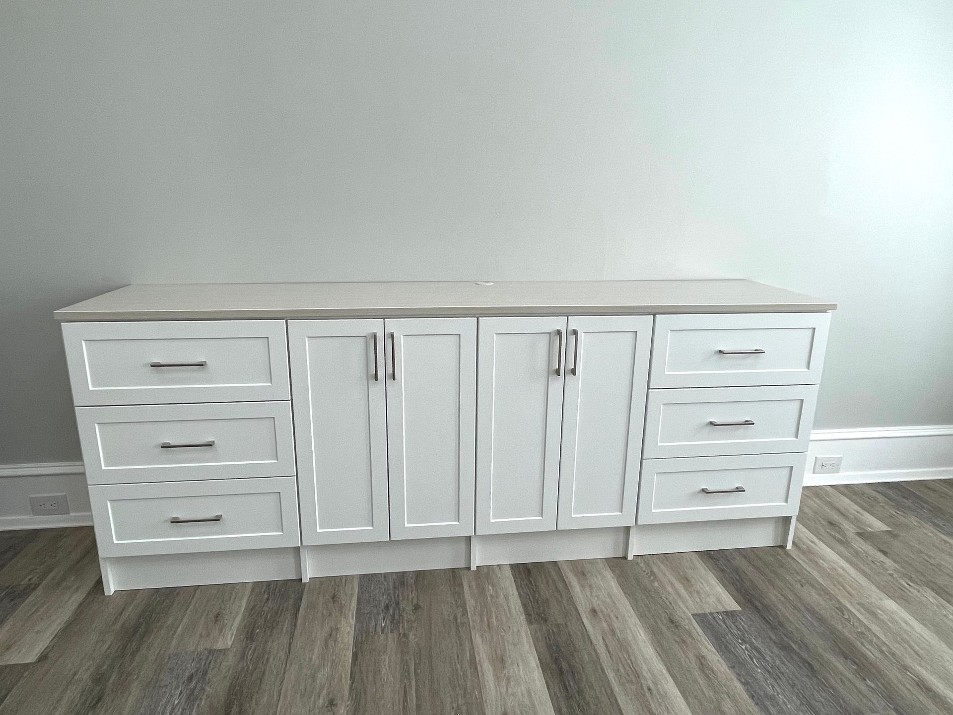 A white cabinet with drawers is sitting on a wooden floor in a room.