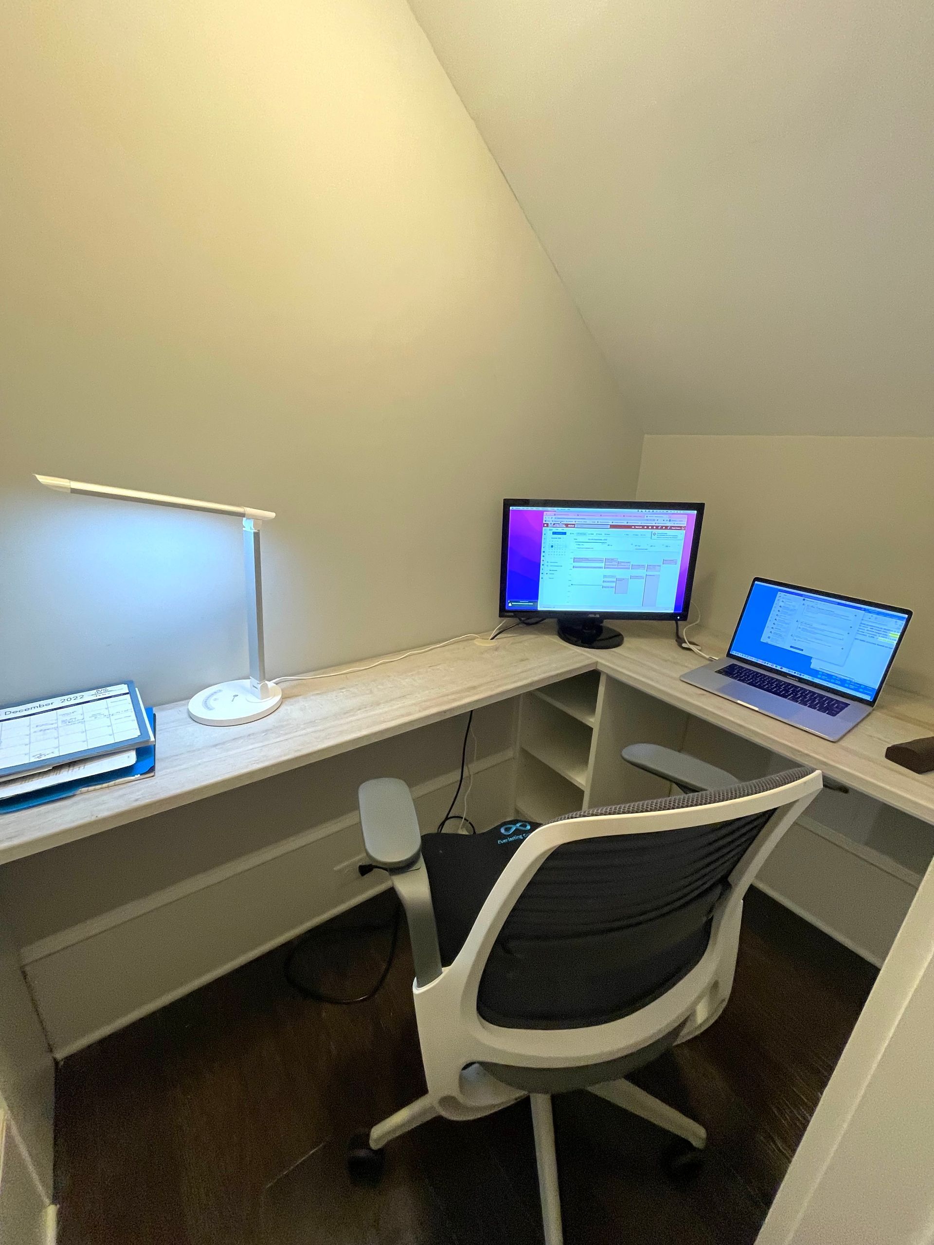 A small office with a desk , chair , computer and laptop.