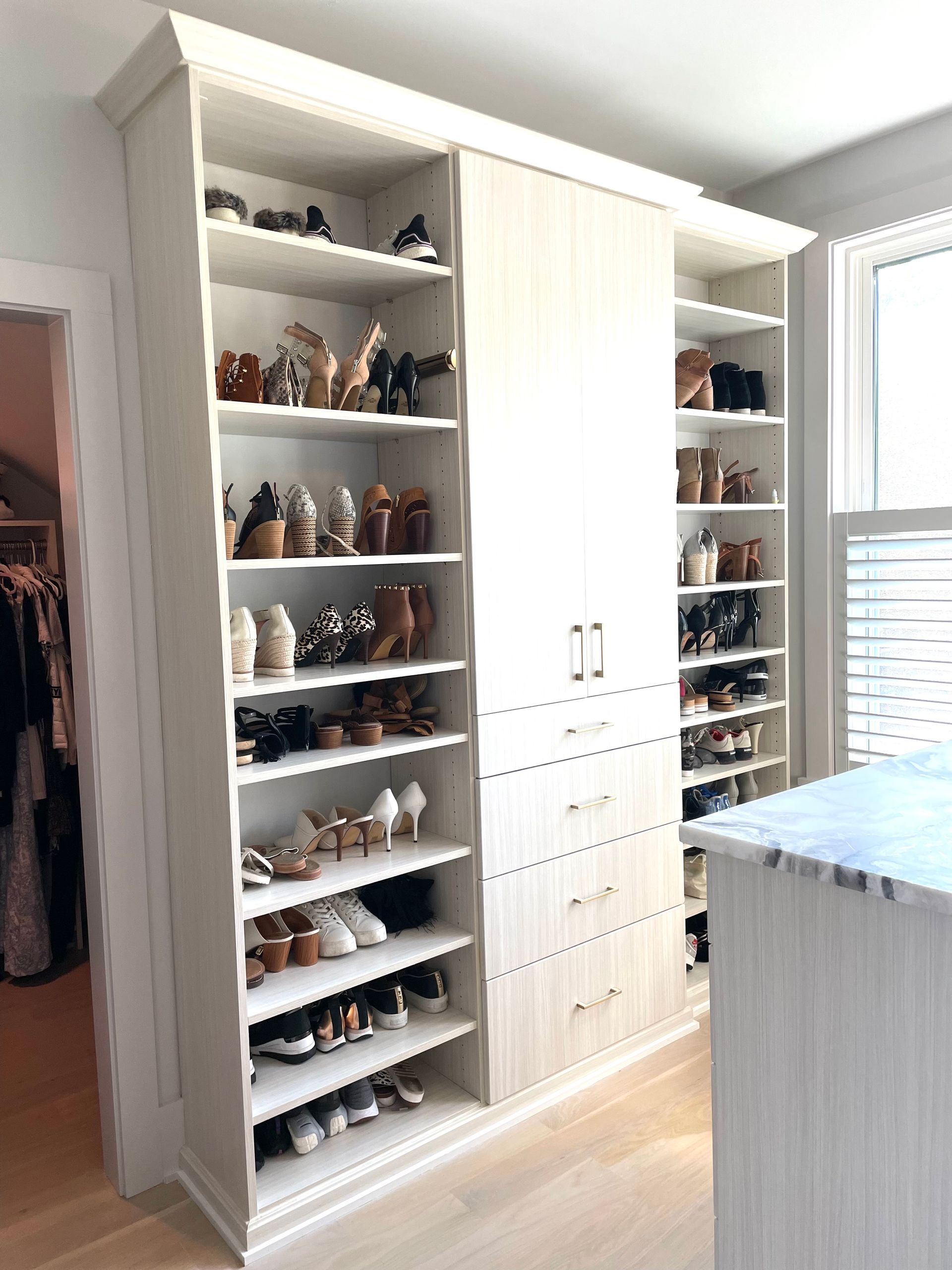 A walk in closet with lots of shelves and drawers filled with shoes.