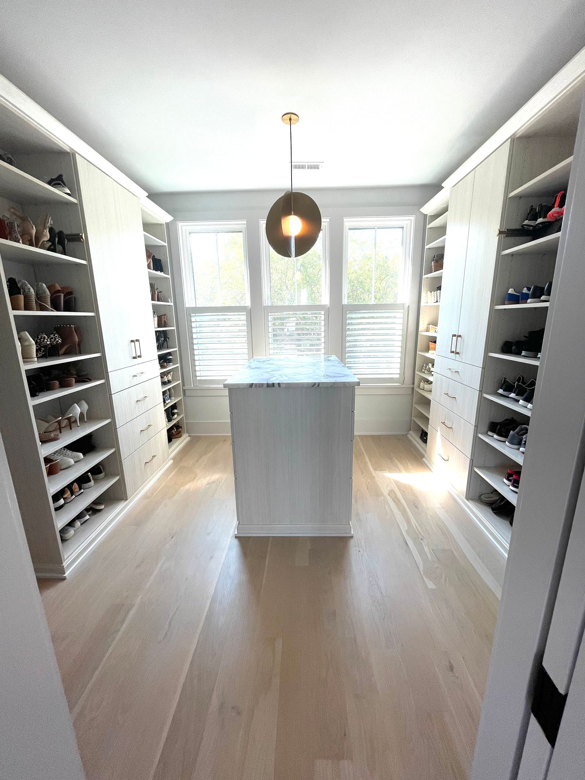 A large walk in closet with lots of shelves and a large island in the middle.