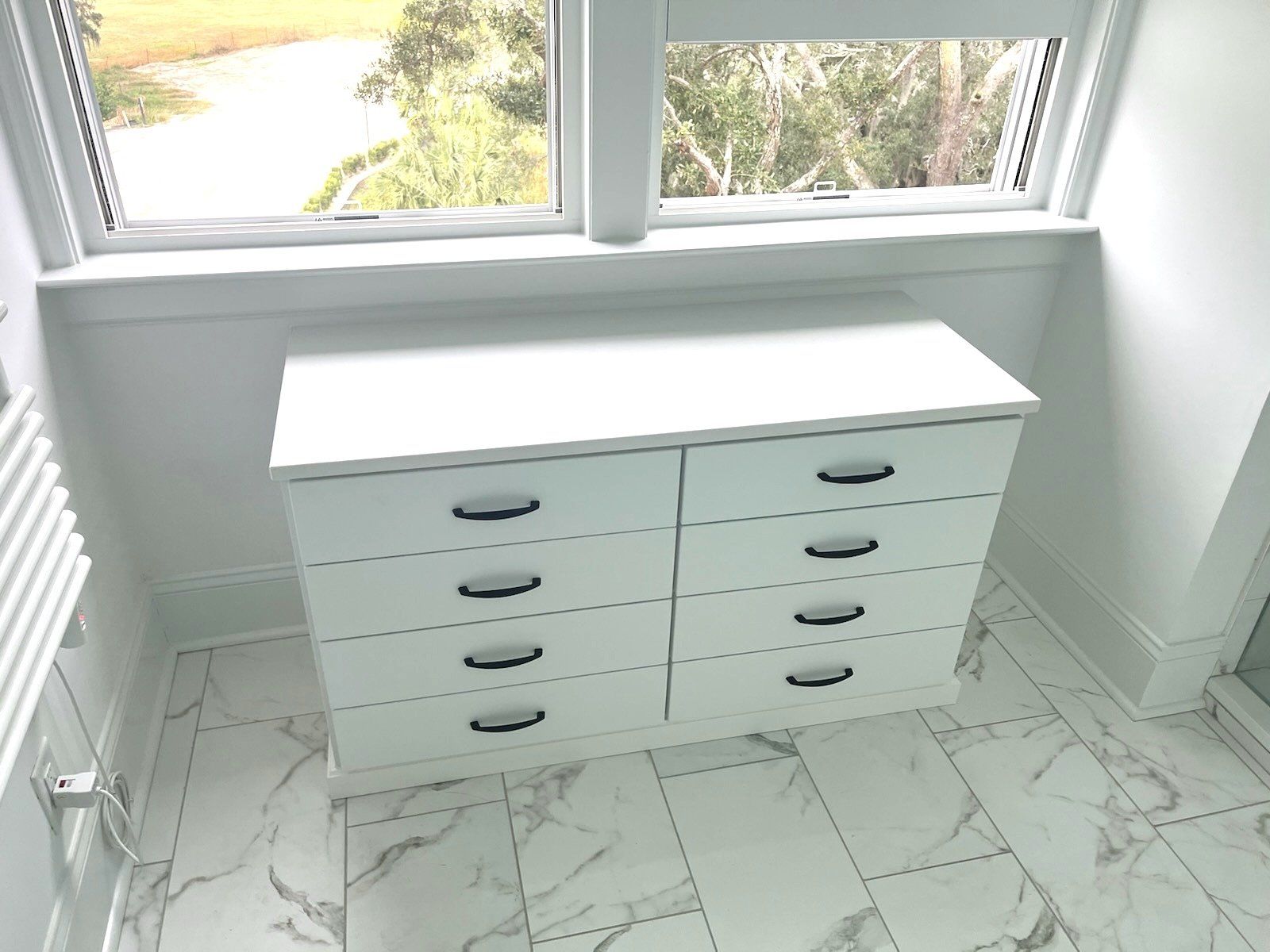 A white dresser is sitting in a room next to a window.