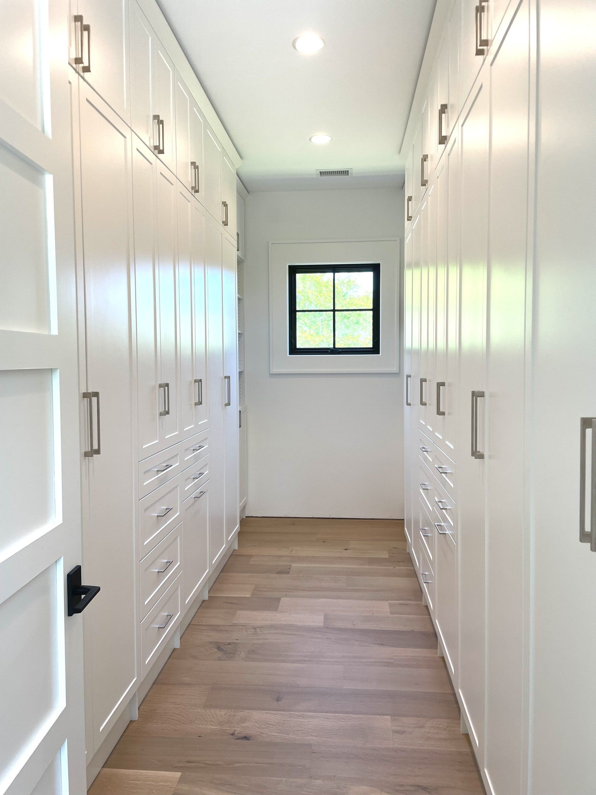 A long hallway filled with white cabinets and drawers and a window.