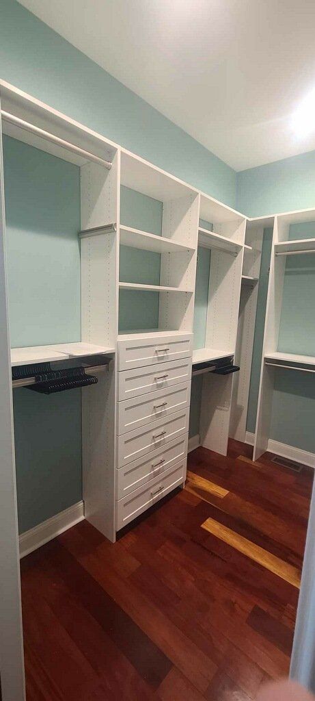 A walk in closet with hardwood floors and white shelves.