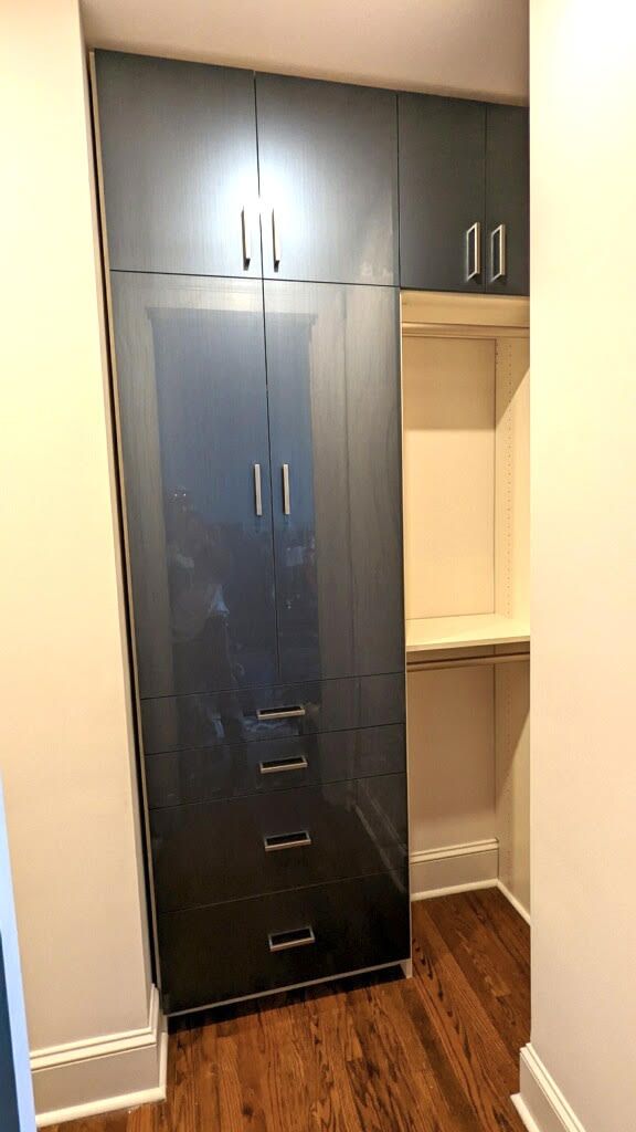 A walk in closet with black cabinets and drawers and a wooden floor.