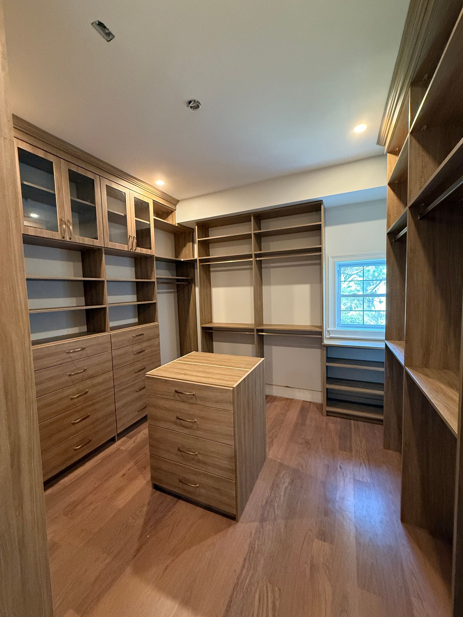A walk in closet with lots of shelves and drawers and a large island in the middle.