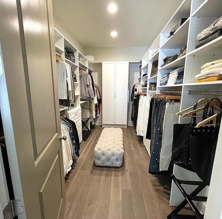 A walk in closet filled with clothes and a white ottoman.