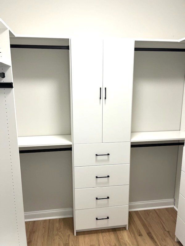 A walk in closet with white cabinets , drawers and shelves.