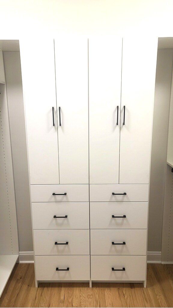 A walk in closet with two white cabinets and drawers.