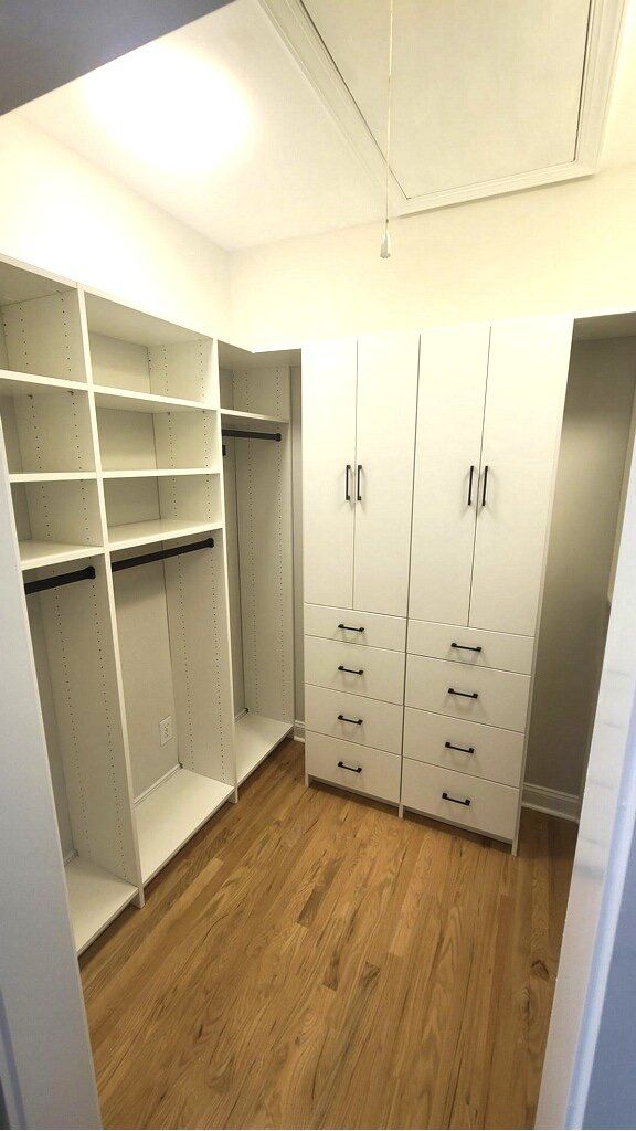 A walk in closet with wooden floors and white shelves.