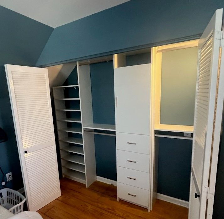A closet with blue walls and white shelves and drawers