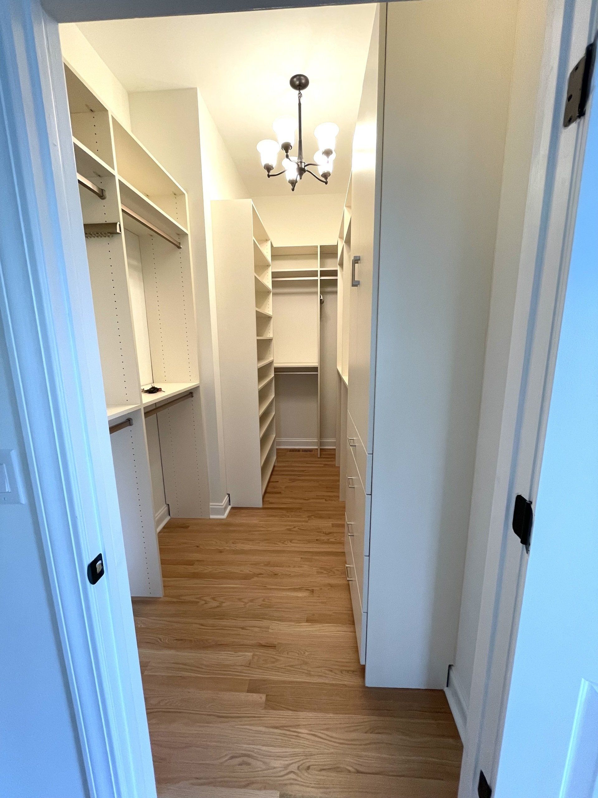 A walk in closet with hardwood floors and white cabinets.