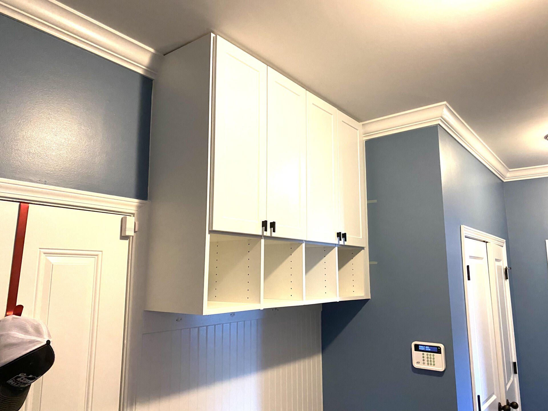 A laundry room with blue walls and white cabinets