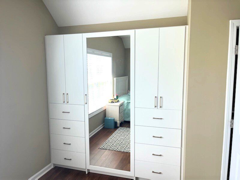A bedroom with white cabinets and drawers and a mirror