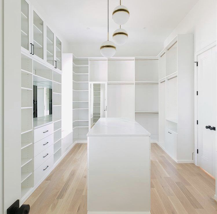 A walk in closet with lots of shelves and drawers and a large island in the middle.