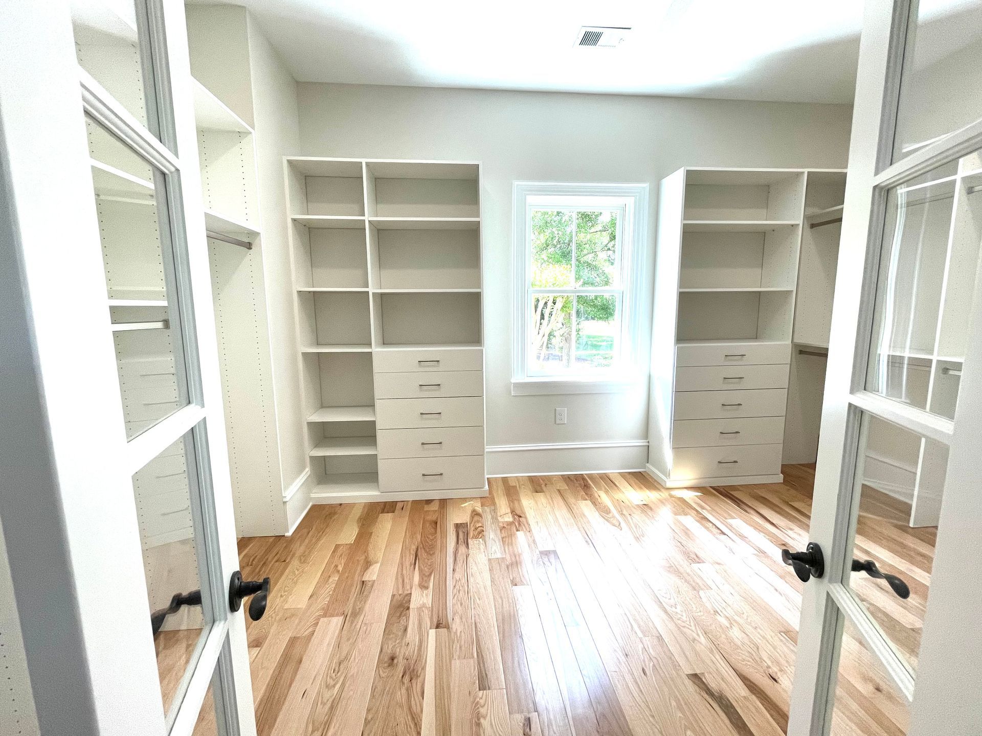 A walk in closet with hardwood floors and white shelves.