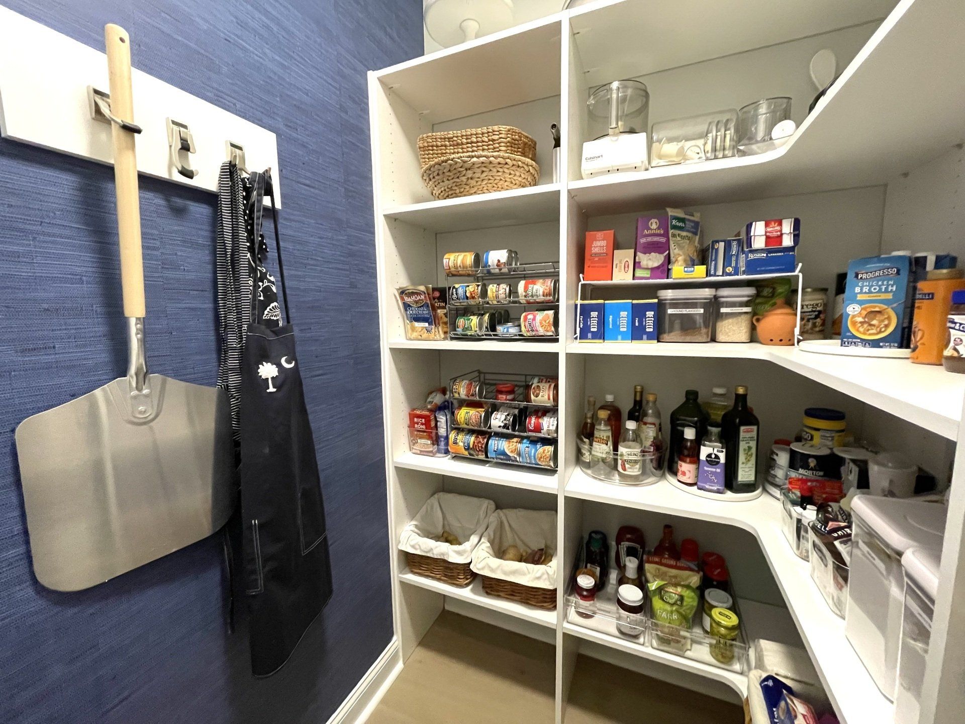 A pantry filled with lots of food and a shovel hanging on the wall.