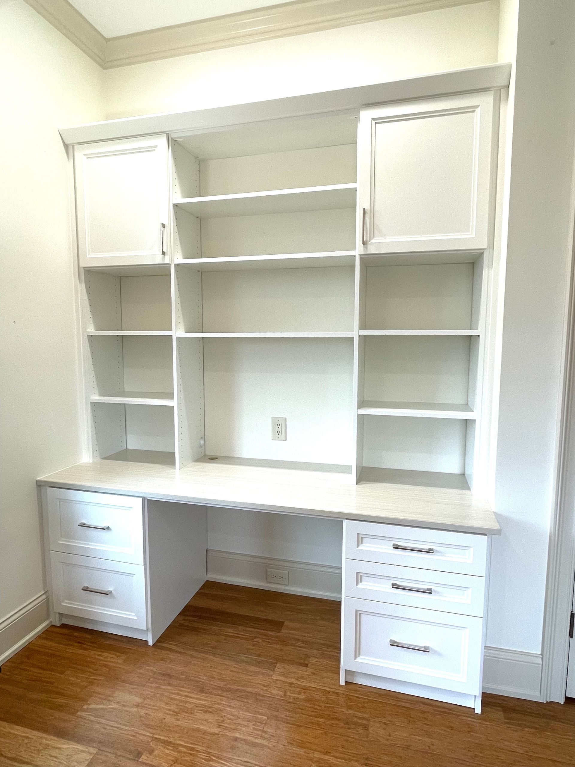 A white desk with drawers and shelves in a room with hardwood floors.