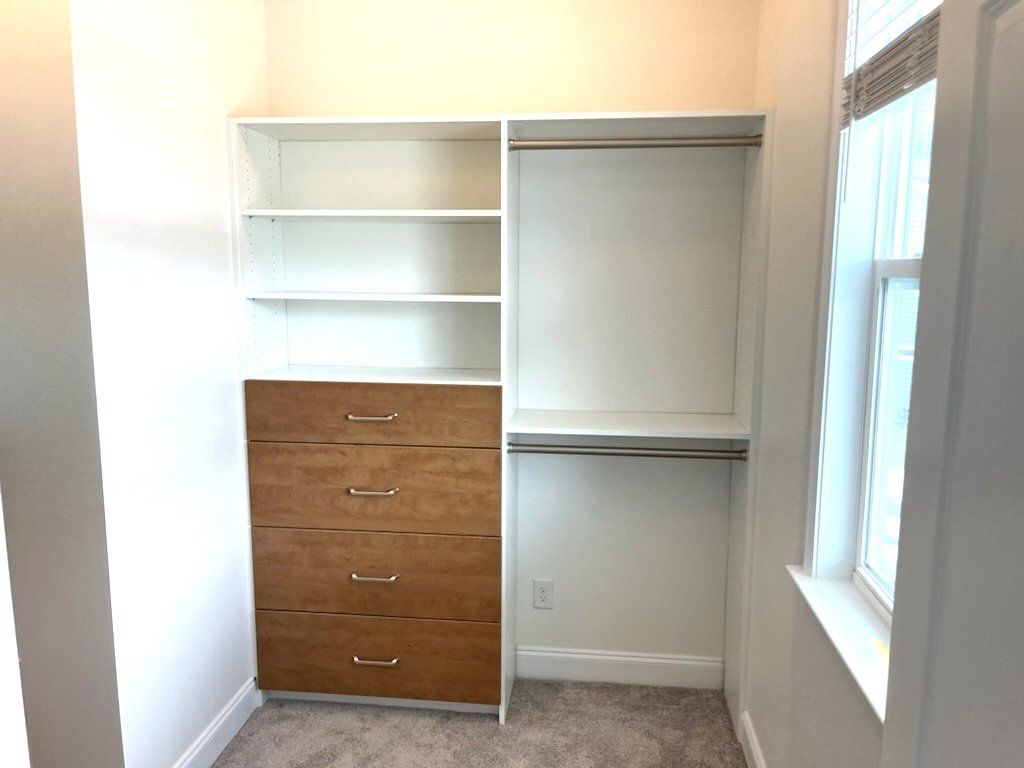 A walk in closet with wooden drawers and shelves and a window.