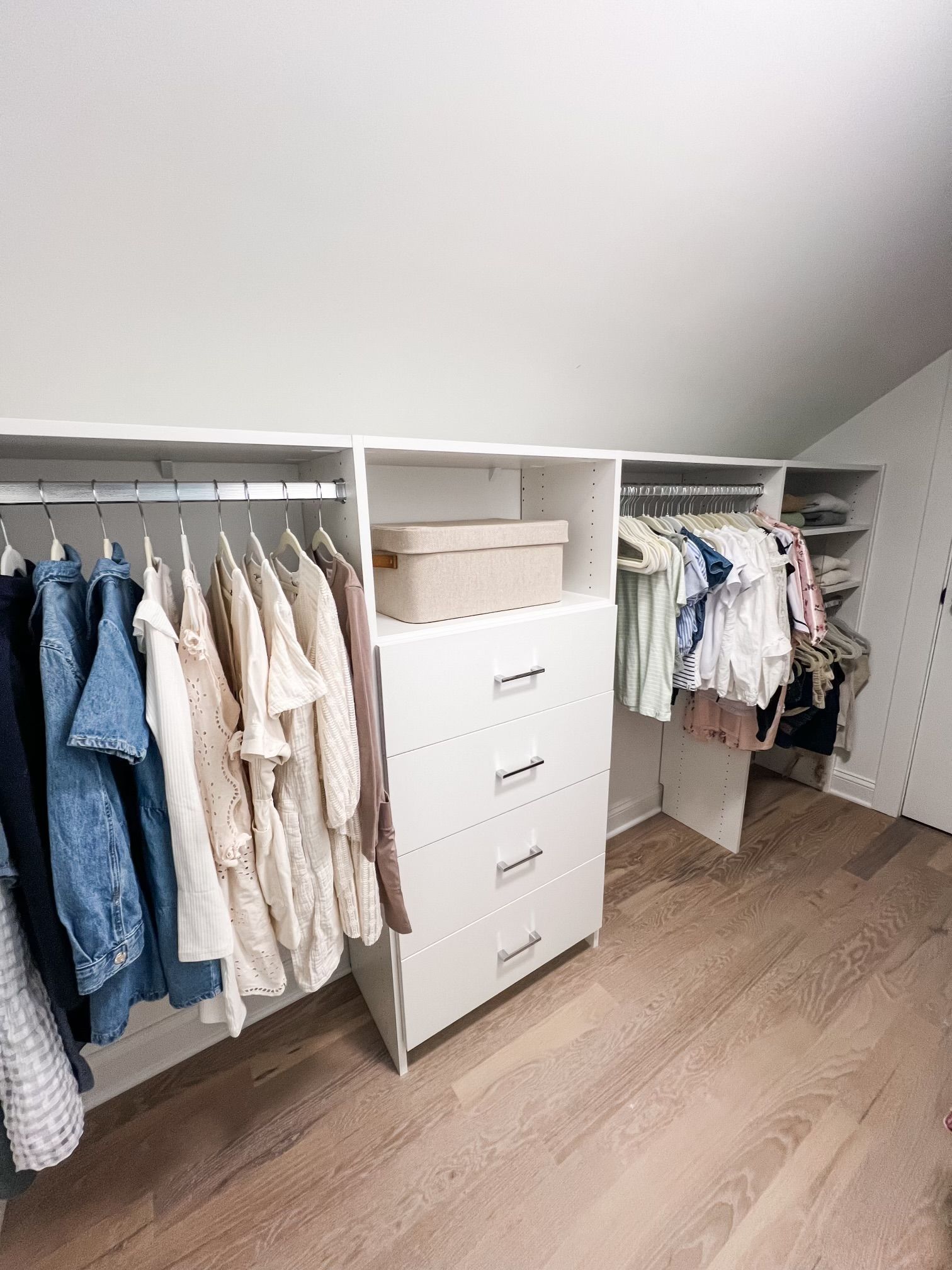 A walk in closet with clothes hanging on racks and a dresser.