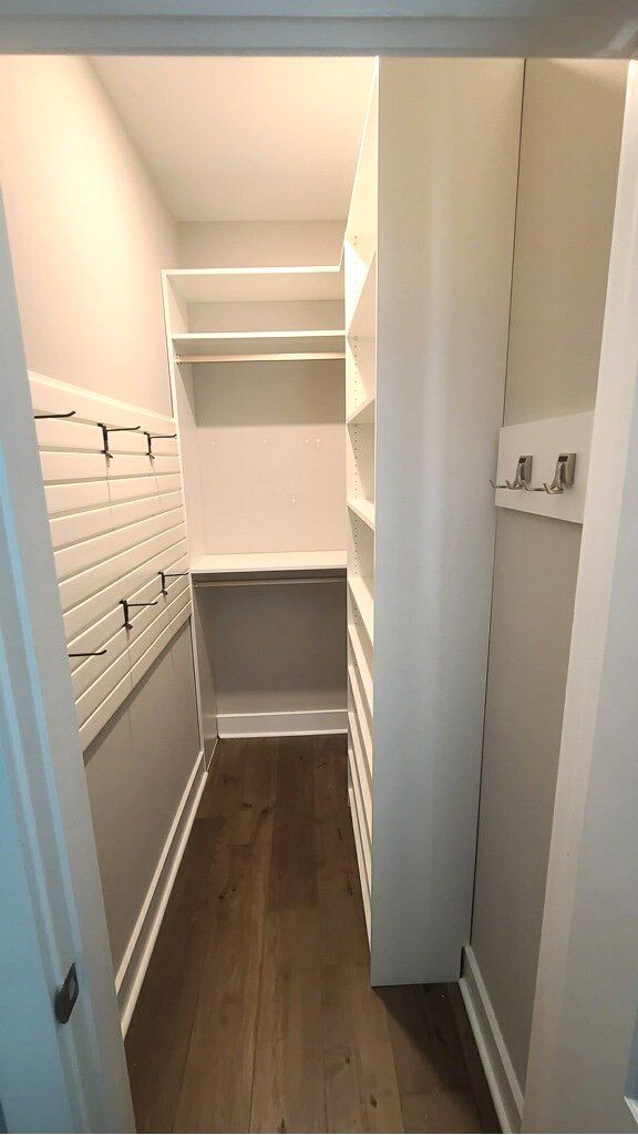 A walk in closet with lots of shelves and hooks on the wall.