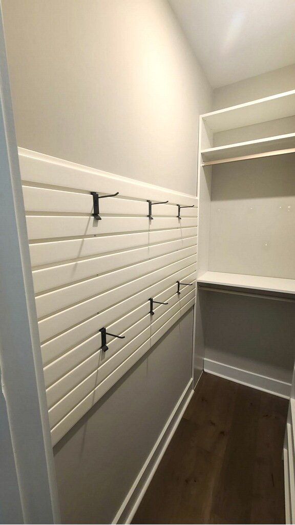 A walk in closet with white shelves and hooks on the wall.