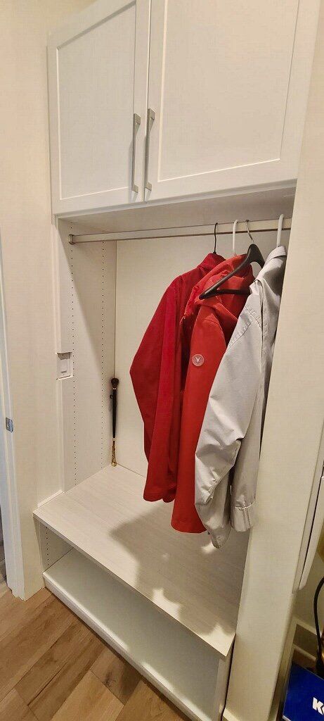 A red jacket and a white shirt are hanging in a closet.