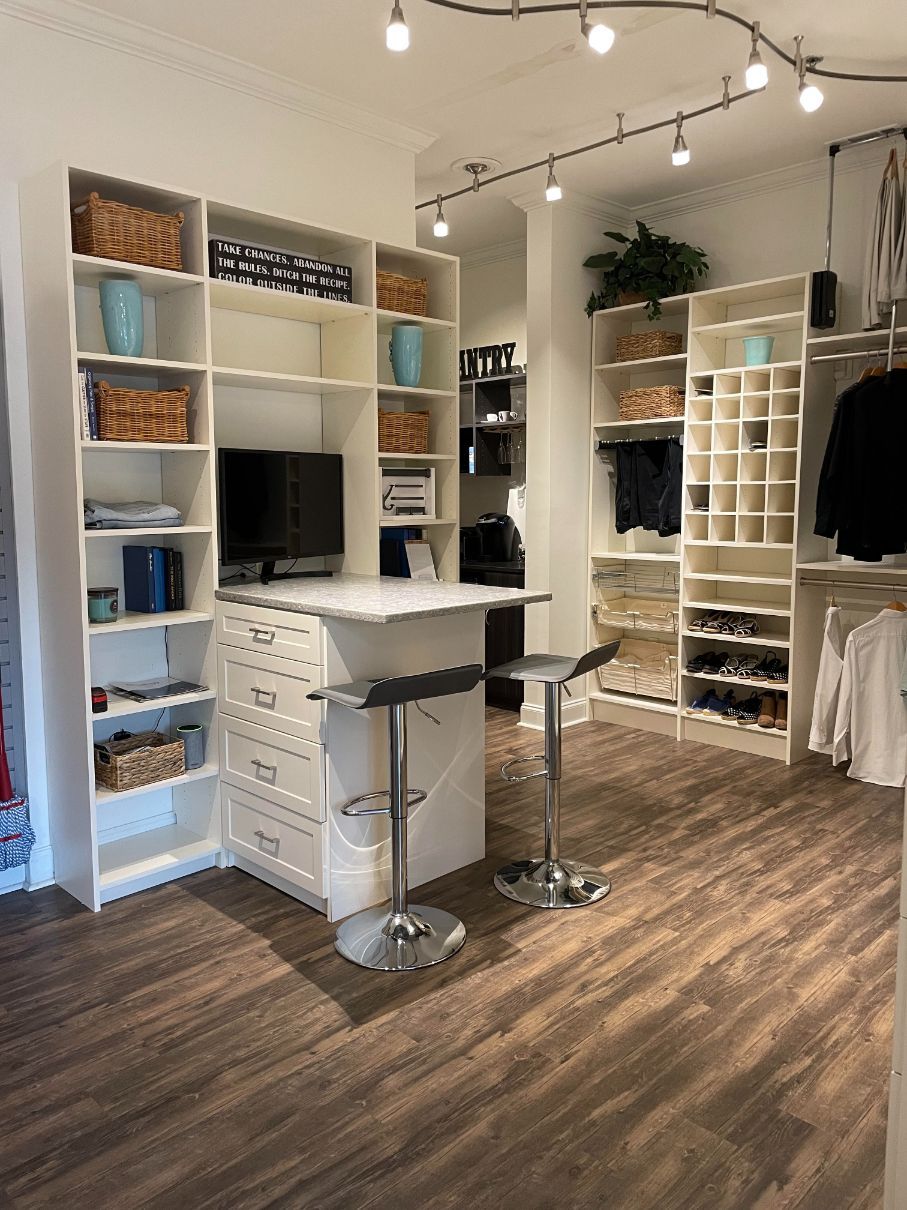 A room with a desk , stools , shelves and a computer.