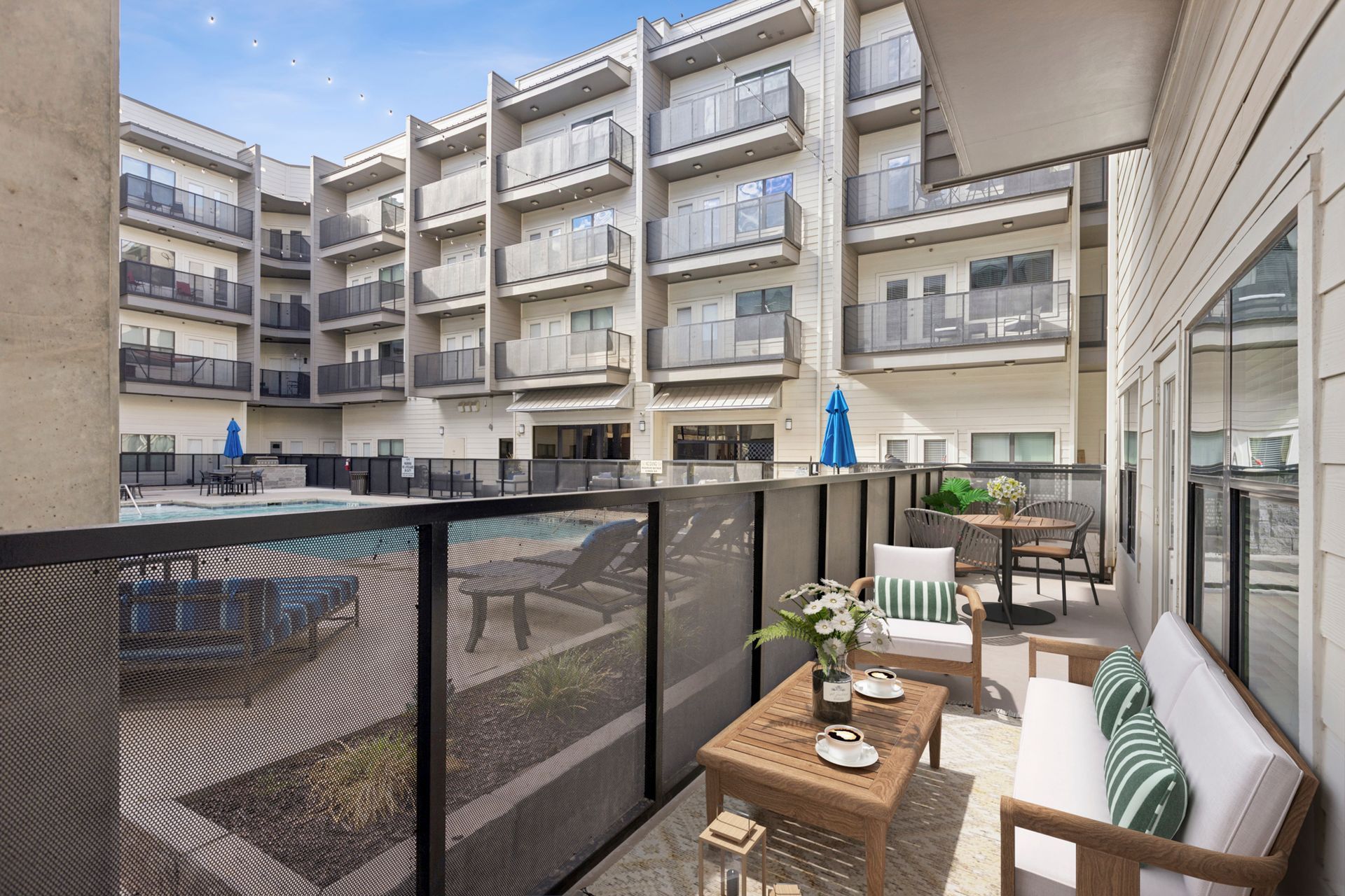 Balcony with furniture overlooking a pool and multi-story apartment building.