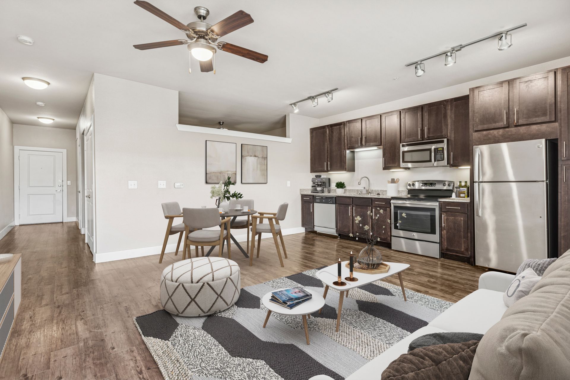 Living room with kitchen, hardwood floors, dining area, and sofa. Brown cabinets, stainless steel appliances.