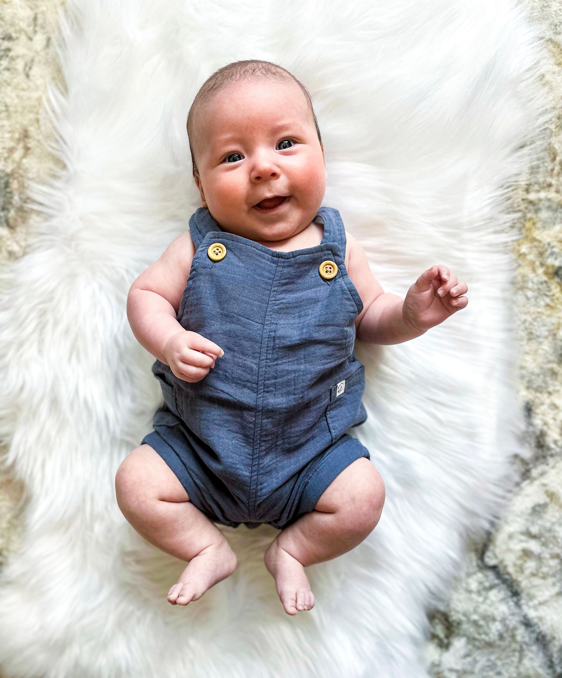 A baby is laying on a white blanket and smiling.