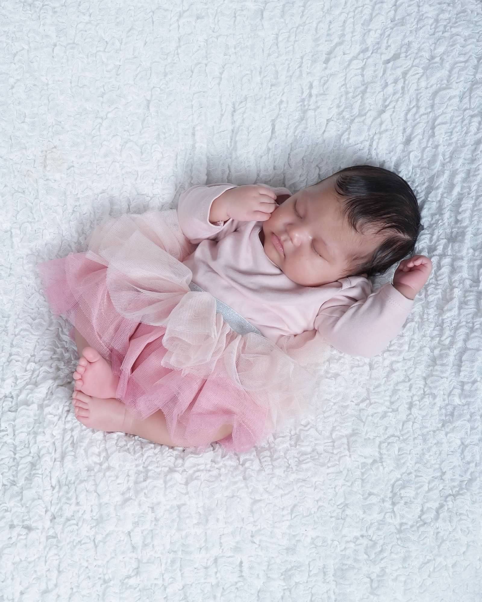 Newborn baby in pink tutu sleeping on a white blanket.