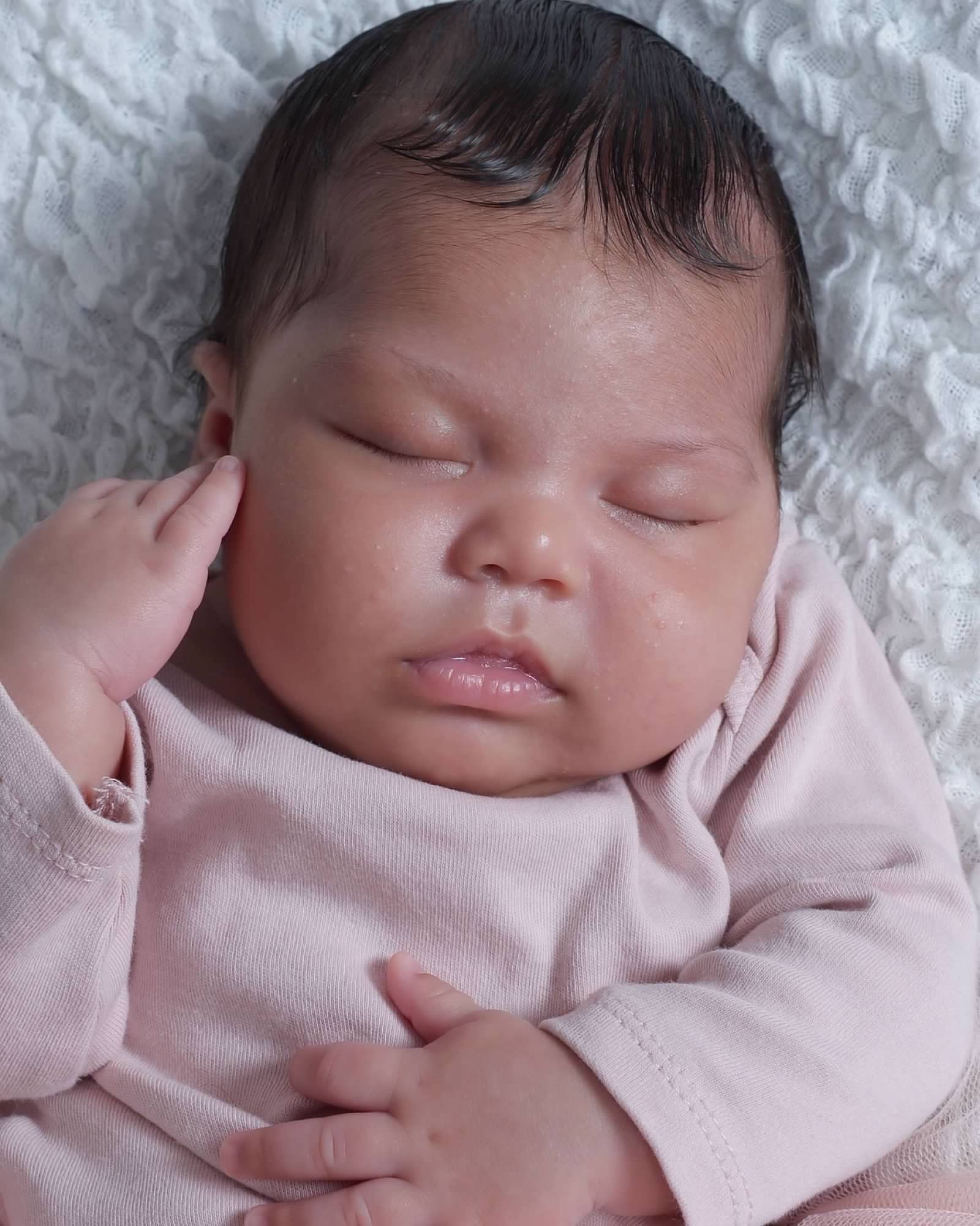 Sleeping baby wearing a pink long-sleeved shirt; resting on a white textured surface.