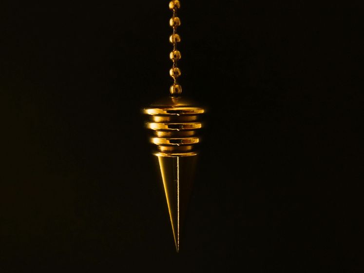 Golden pendulum hanging against a black background.
