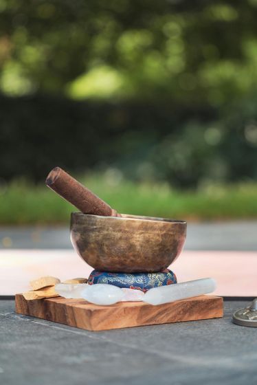 Bronze singing bowl with mallet, on a wood block, outdoors, green background.