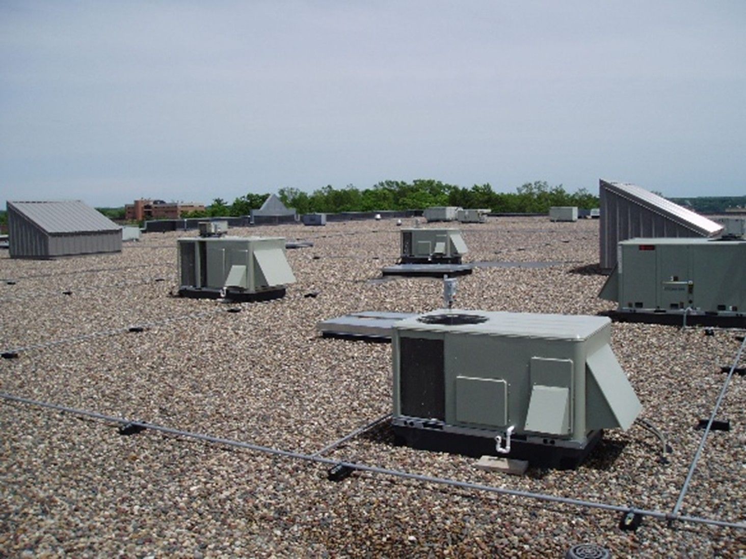 Rooftop with several HVAC units on a gravel surface under a clear sky