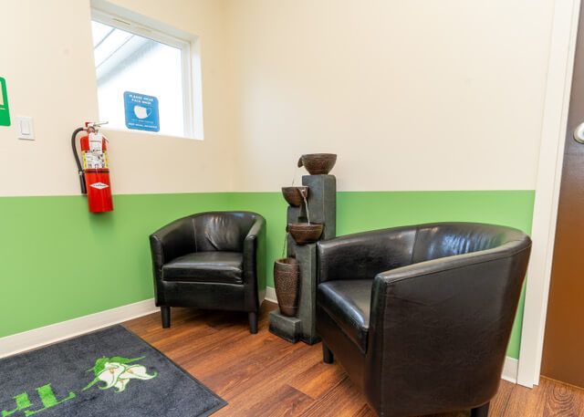 Two black leather chairs and a water fountain in a waiting area with a fire extinguisher and window.