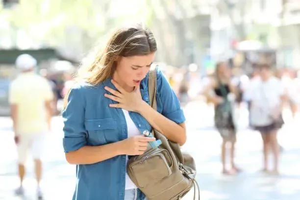 A woman stands in the street, holding her chest, visibly struggling with an asthma attack.