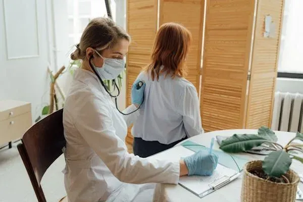 A woman in a white coat sits at a table with a stethoscope, symbolizing care for asthma patients.