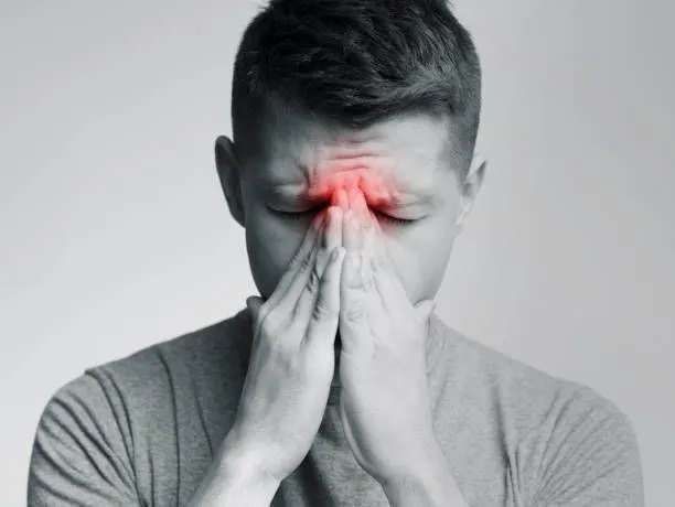 A person holds their forehead, with a red spot indicating pain or headache due to sinusitis.