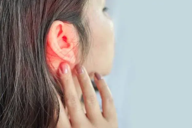 A woman holding her ear in discomfort, indicating pain, with a pained expression on her face.