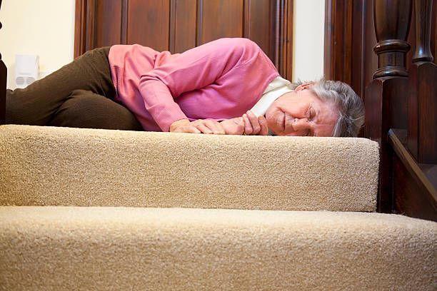 An older woman lies on the stairs, appearing to have slipped and fallen, with a concerned expression