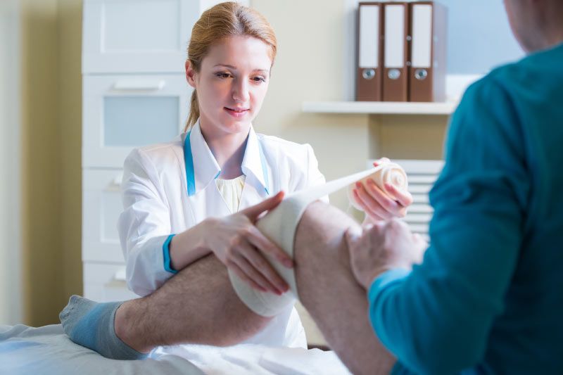 A doctor is bandaging a patient 's knee in a hospital.