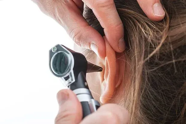 Individual using a hearing aid while performing an ear checkup for better auditory health.