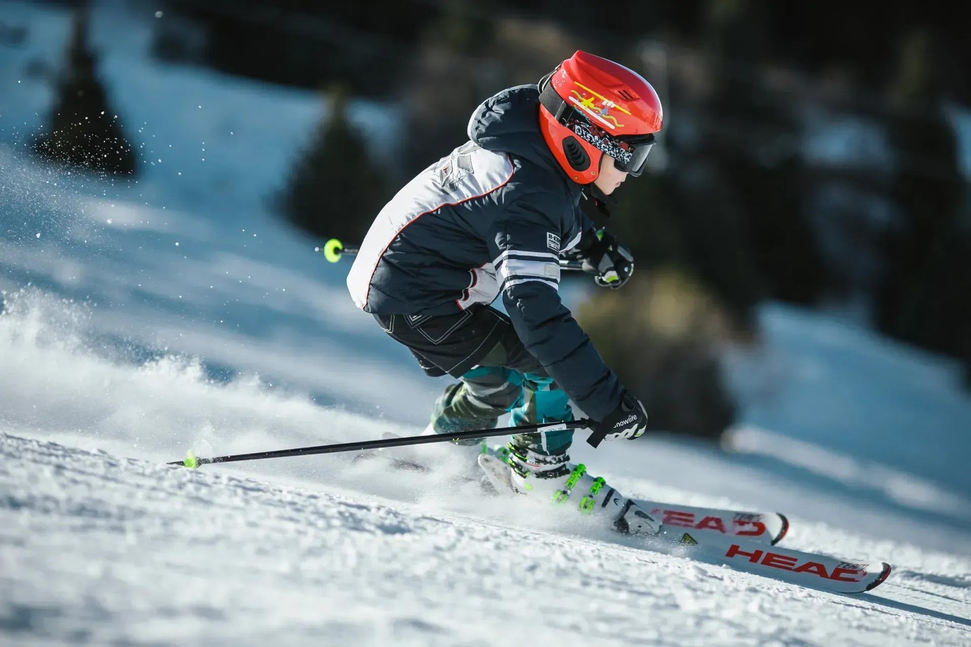 A young skier in a helmet and jacket descends a snowy slope, emphasizing winter sports safety and sk