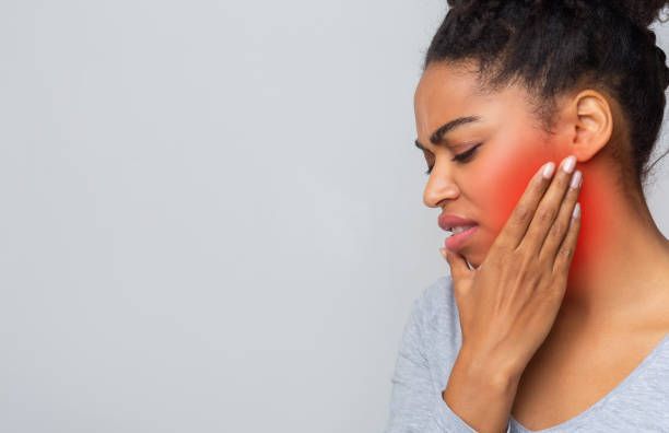 A woman grimaces in pain, holding her jaw, indicating a severe toothache possibly linked to sepsis.