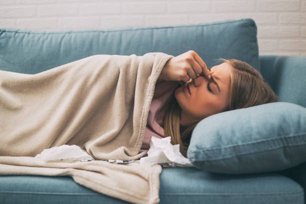 A woman lying in bed, holding her nose in discomfort, struggling with the pain and congestion.